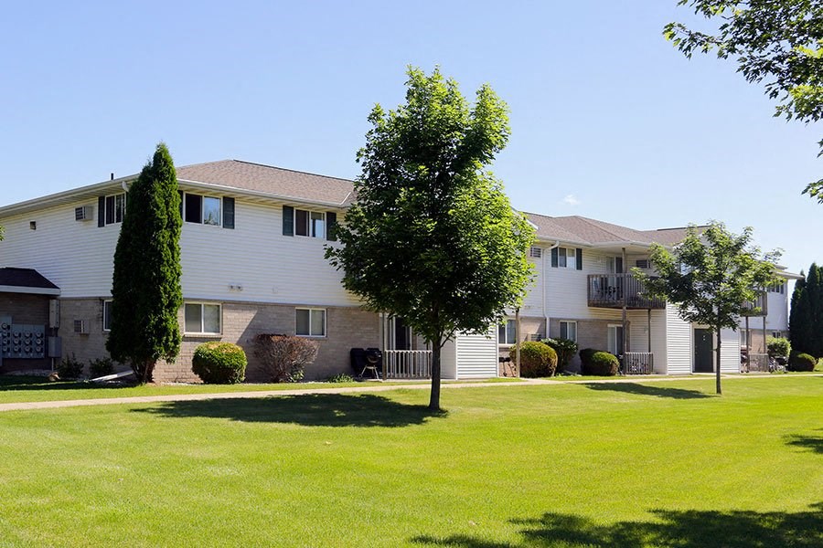 a white building with a green lawn and trees