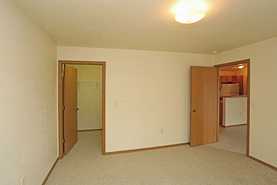 an empty room with a mirror and a door to a kitchen
