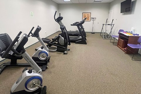 A gym room with exercise equipment and a TV.