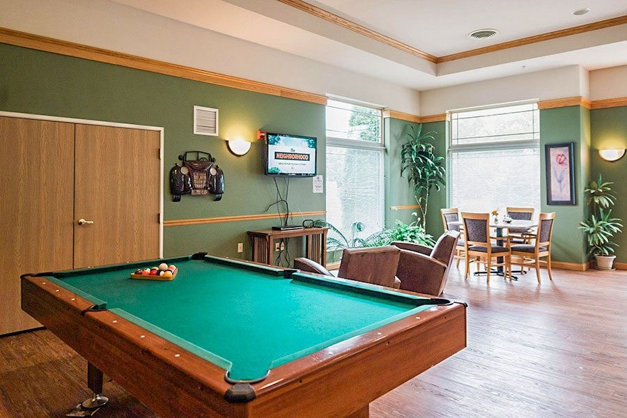 A pool table is in the middle of a room with a TV mounted on the wall.
