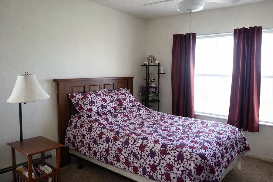 A bed with a floral patterned comforter sits in a room with a window and curtains.