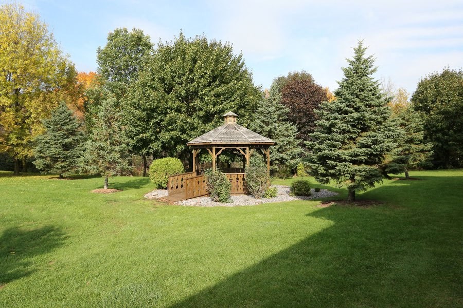A gazebo sits in the middle of a lush green lawn.