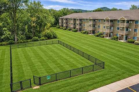 A black fence surrounds a green lawn in front of apartment buildings.