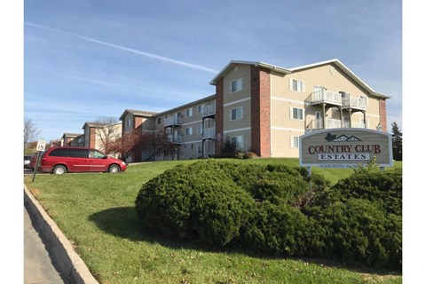 a red car parked in front of a community club estates sign