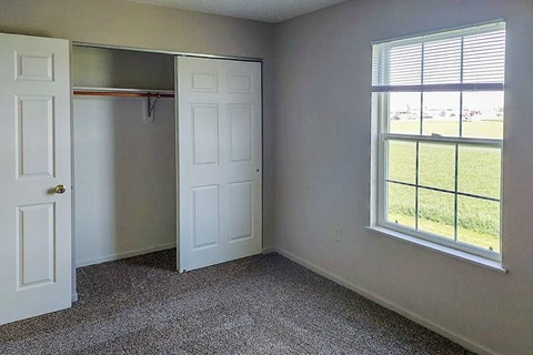 A room with a grey carpet, a white door, a white wardrobe and a window with blinds.
