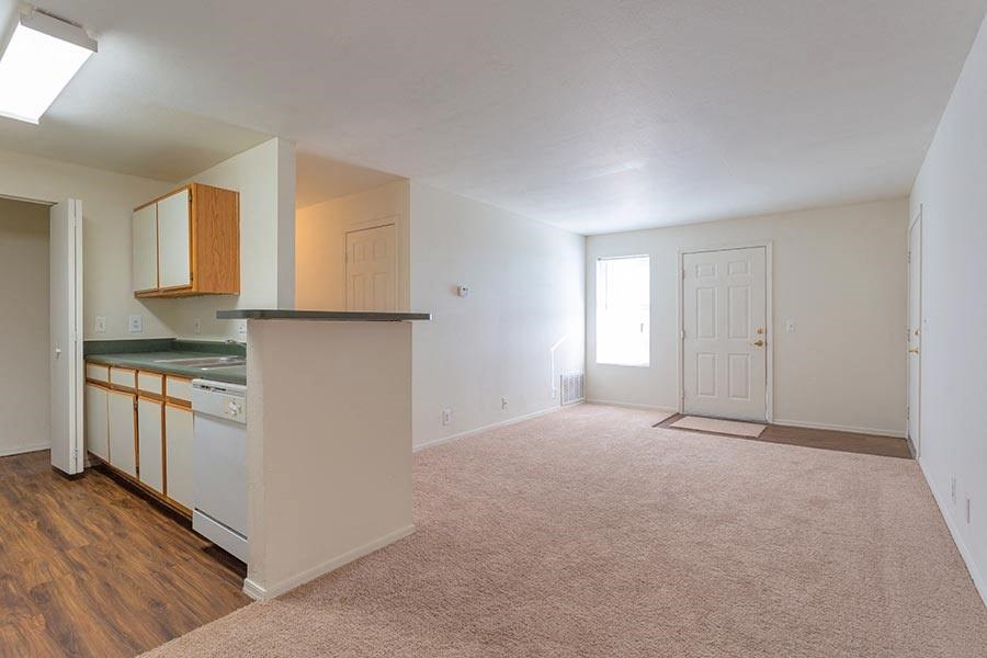 an empty living room with a kitchen and a door