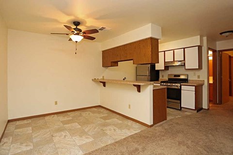 an empty living room with a kitchen and a ceiling fan