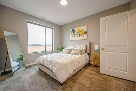 A bedroom with a large bed, a mirror, a painting, and a window.