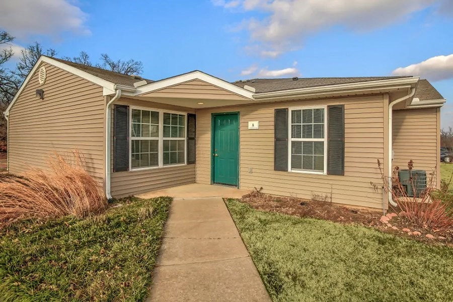 a small tan house with a green door and a sidewalk