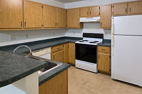 A kitchen with a white fridge, black stove and wooden cabinets.