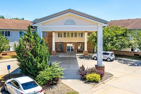 A white car is parked in front of a building with a covered walkway leading to the entrance.