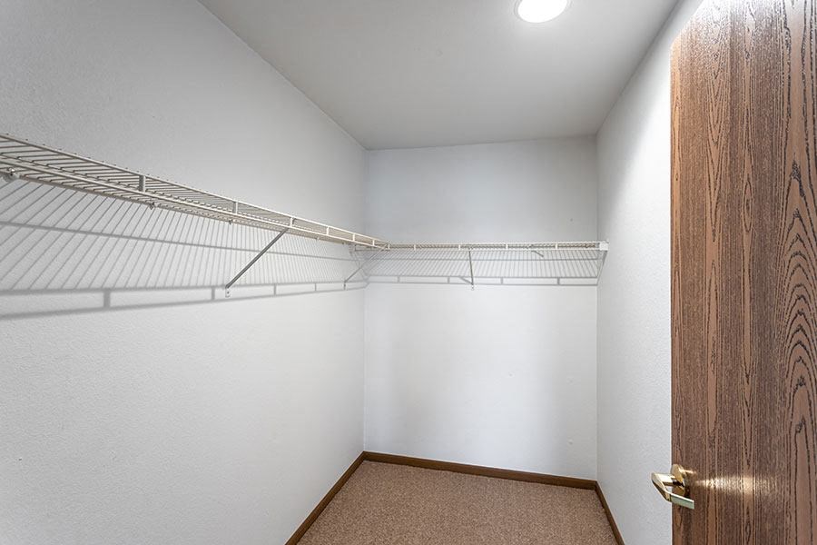 A walk-in closet with a brown carpet and a wooden door.