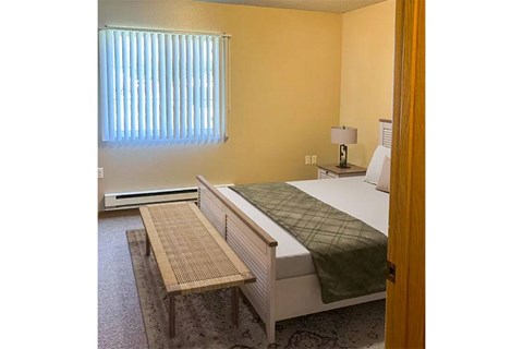 A bedroom with a bed, nightstand, and window with blinds.