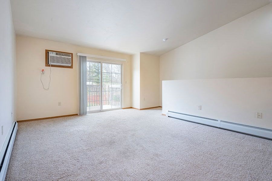 A room with a carpeted floor and a window with a sliding glass door.