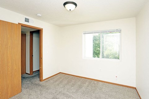 A room with a carpeted floor, a window, and a wooden door.
