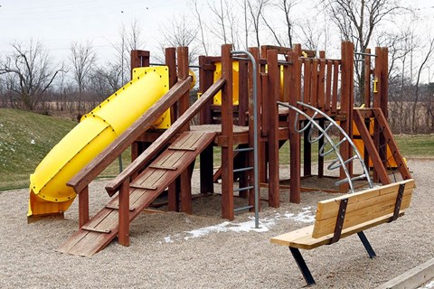 a playground with a yellow slide and wooden benches