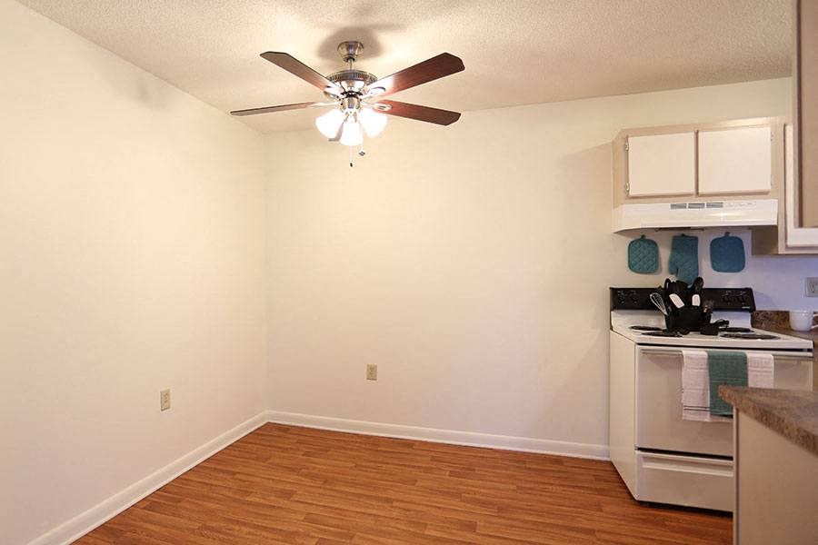 an empty room with a ceiling fan and a kitchen