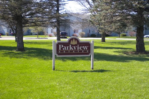 a park sign in the grass in front of a house