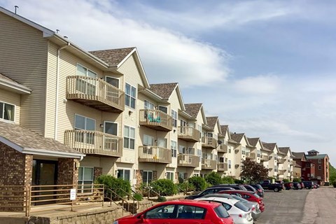 A red car is parked in front of a building with a balcony.