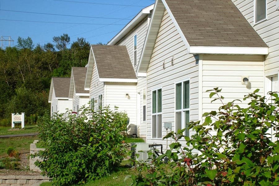 A white house with a brown roof is surrounded by greenery.
