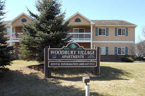 A sign for Woodbury Village Apartments in front of a building.