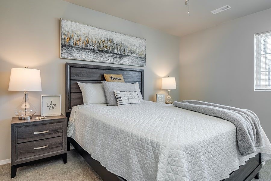 A bedroom with a large bed, a nightstand with a lamp, and a framed picture on the wall.