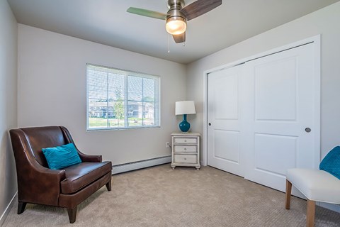 A brown leather chair with a blue pillow sits in a room with a ceiling fan and a white door.