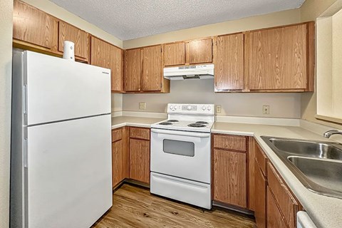 A white refrigerator stands in a kitchen with wooden cabinets and a white stove.