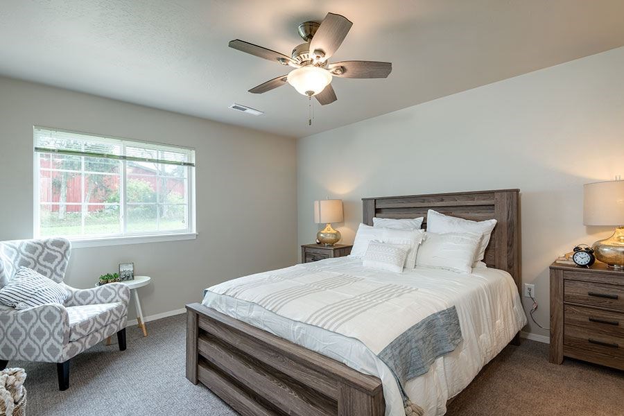 A bedroom with a bed, chair, and ceiling fan.