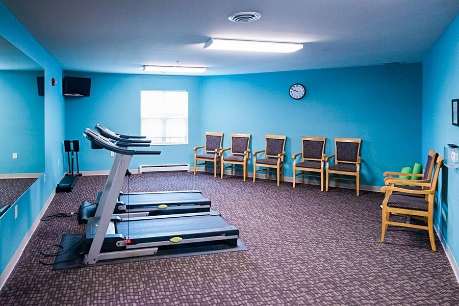 A room with a treadmill, chairs, and a clock on the wall.
