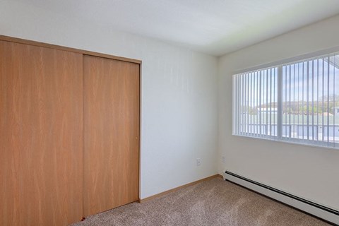 an empty bedroom with a window and a wooden closet