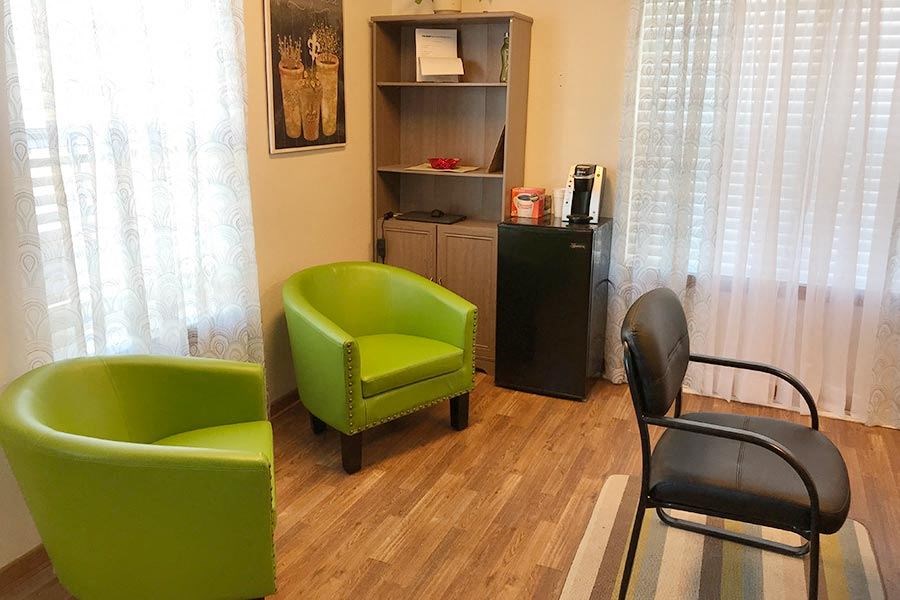 A room with a green chair, a black chair and a shelf with books and a vase.