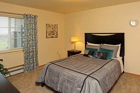 A bedroom with a large bed and a window with curtains.