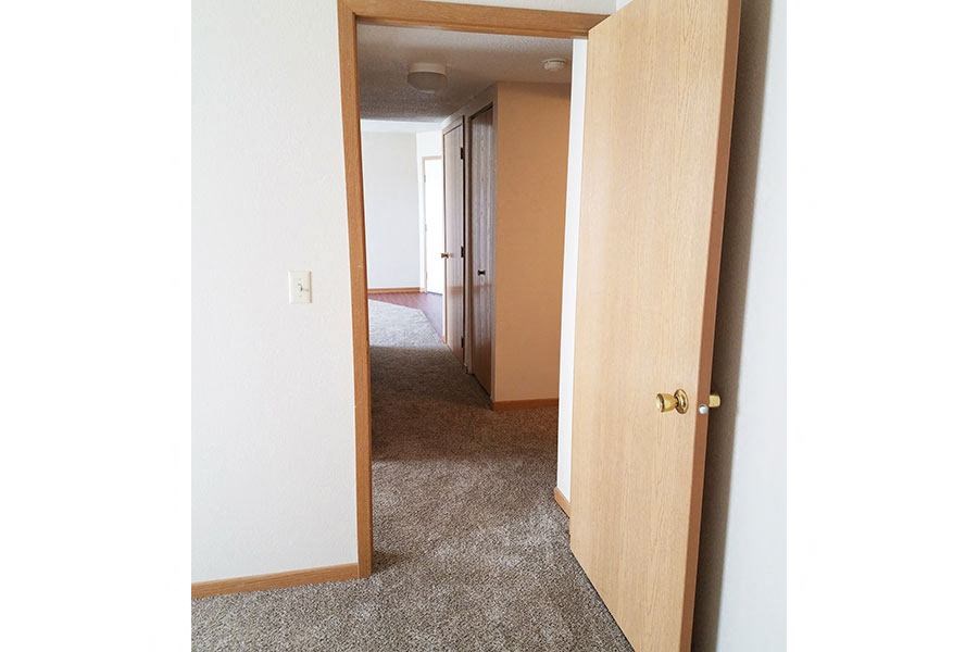 A white door with a gold handle is open to a hallway.