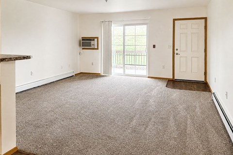 A spacious living room with a carpeted floor and a sliding glass door leading to a balcony.