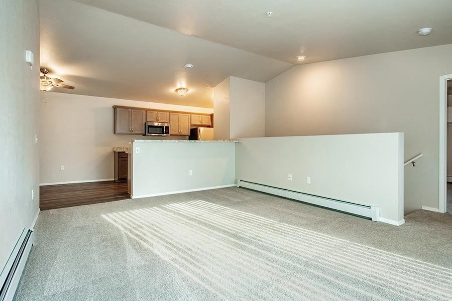 an empty living room with a kitchen in the background