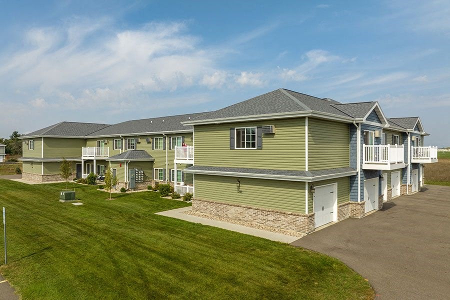 a row of green houses with a lawn and a driveway