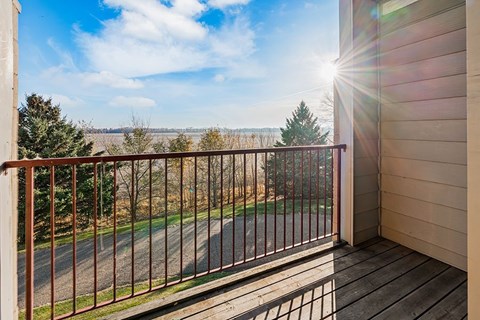 A balcony with a metal railing overlooking a road and trees.