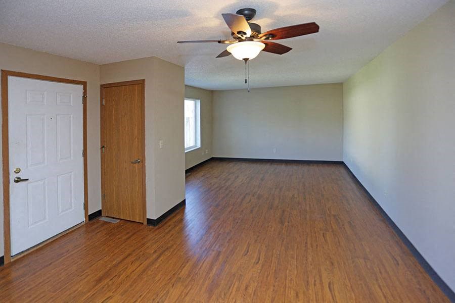 an empty living room with wood floors and a ceiling fan