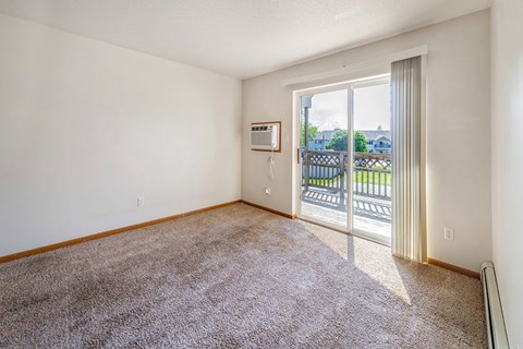 A room with a carpeted floor and a sliding glass door leading to a balcony.