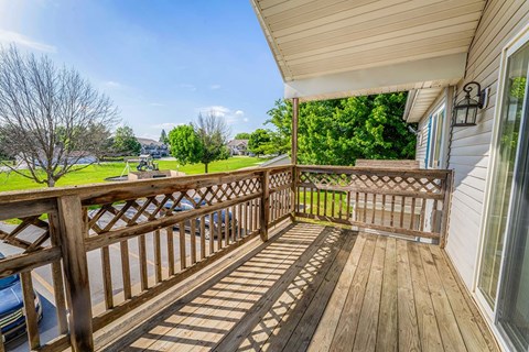 A wooden deck with a railing and a view of a grassy area and trees.