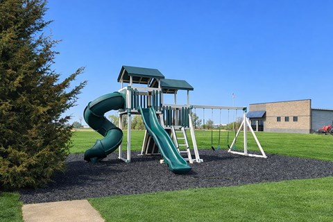 A green and white playground with a slide and a swing set.