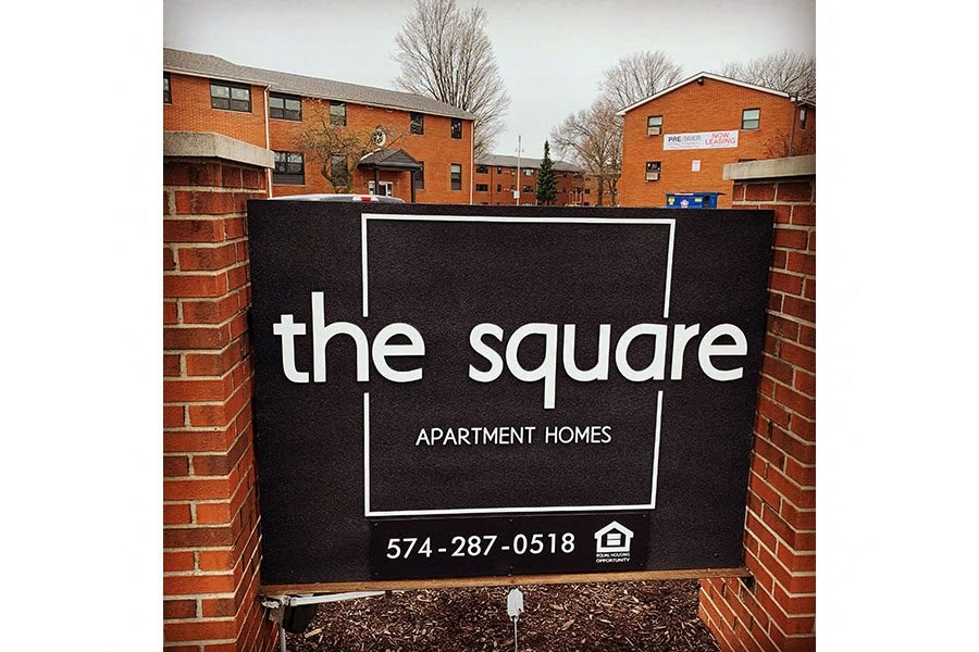 A sign for "The Square Apartment Homes" is displayed in front of a brick wall.