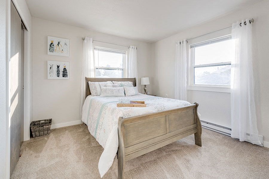 A bedroom with a bed, two windows, and a basket on the floor.