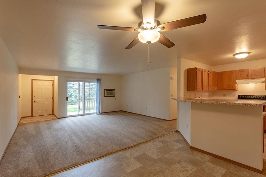 an empty living room and kitchen with a ceiling fan
