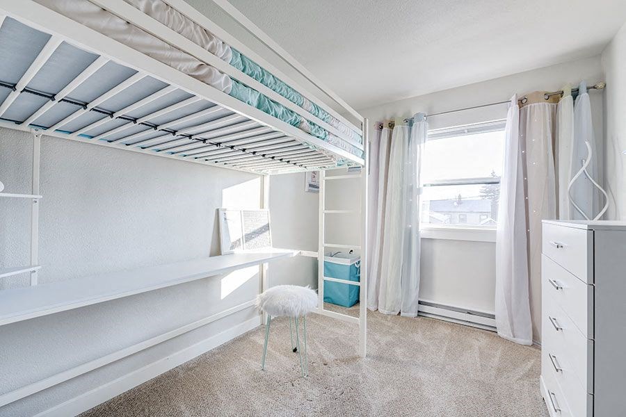 A white room with a bed under a skylight and a white chair.