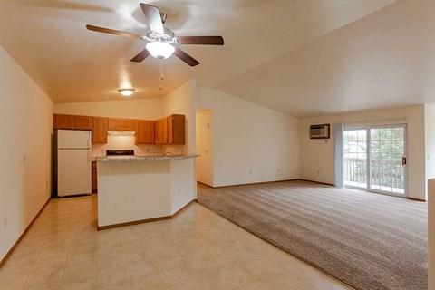 an empty living room with a kitchen and a ceiling fan