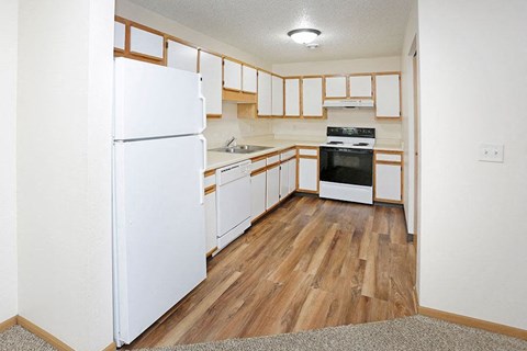 an empty kitchen with white appliances and wood floors