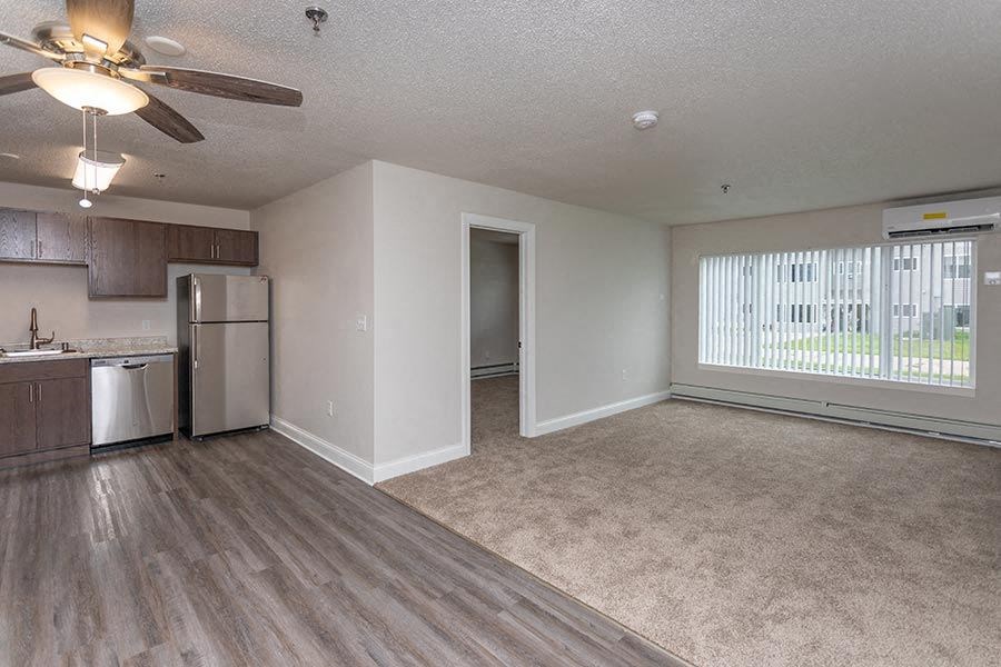 an empty living room with a kitchen and a ceiling fan