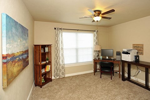 a living room with a desk and a ceiling fan